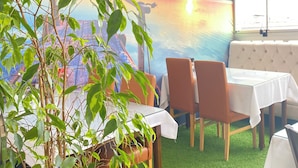 A restaurant with a mural of a sunset over water, green plants, and a seating area with tables and chairs. - Polanin Hotel (Istanbul)