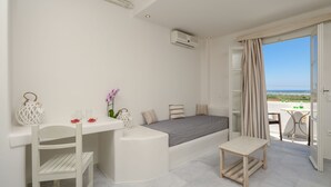 A modern bedroom with a bed, a small table, a chair, and a view of the sea. - Agnanti Hotel (Naxos)