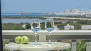A table with two glasses of water and two green apples, overlooking a coastal view with buildings in the distance. - Agnanti Hotel (Naxos)
