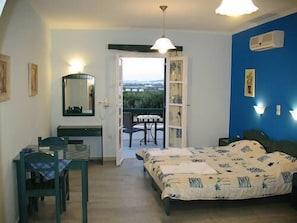 A bedroom with a bed, a desk, and a chair. There is a balcony with a view of the outside. - Agnanti Hotel (Naxos)