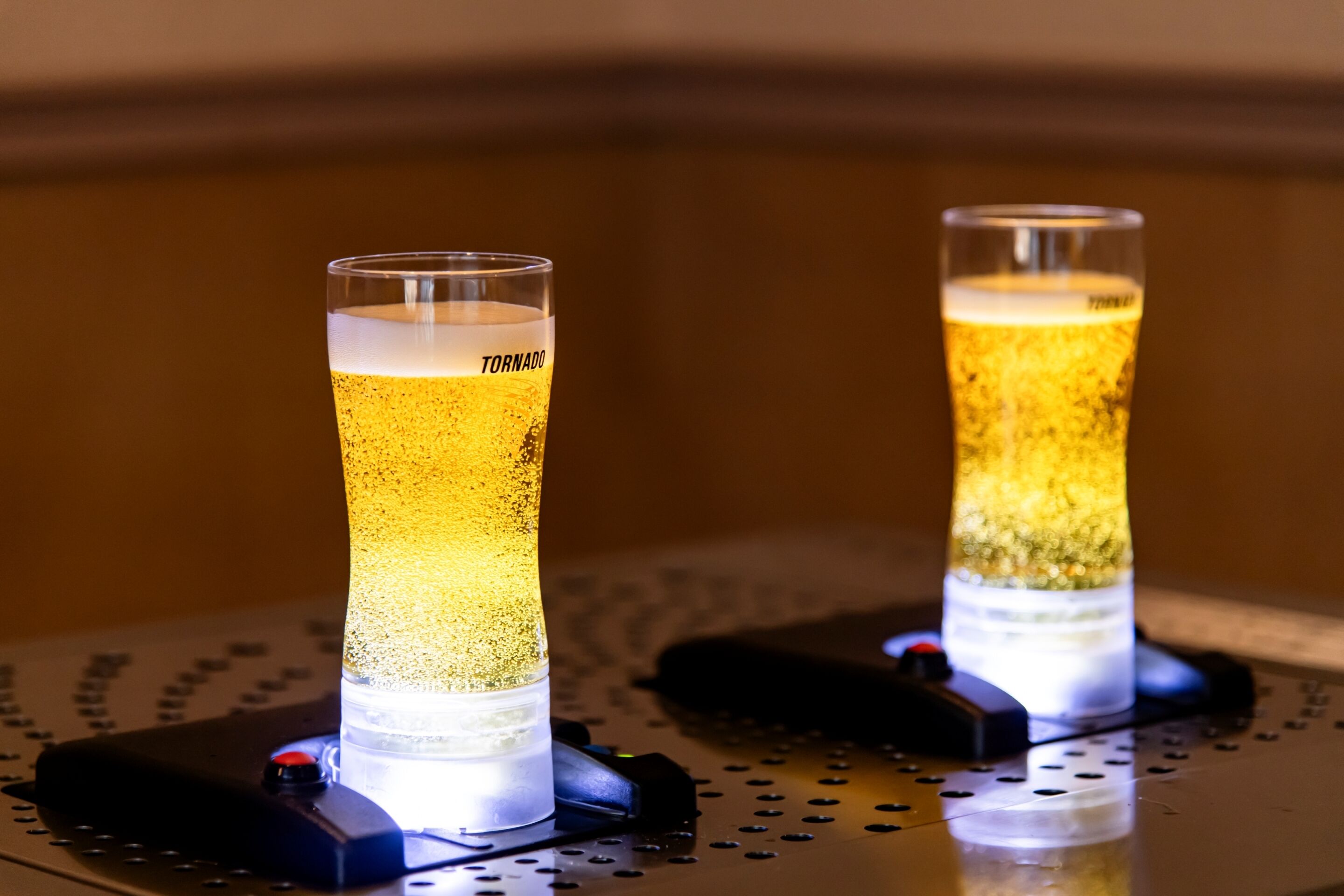 Two illuminated glasses of beer on a metal surface with a perforated pattern.
