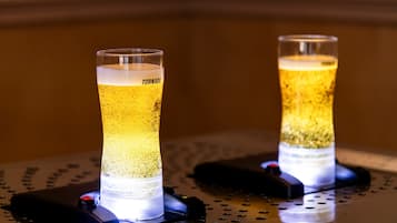 Two illuminated glasses of beer on a metal surface with a perforated pattern.