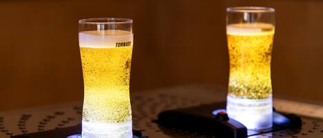 Two illuminated glasses of beer on a metal surface with a perforated pattern.