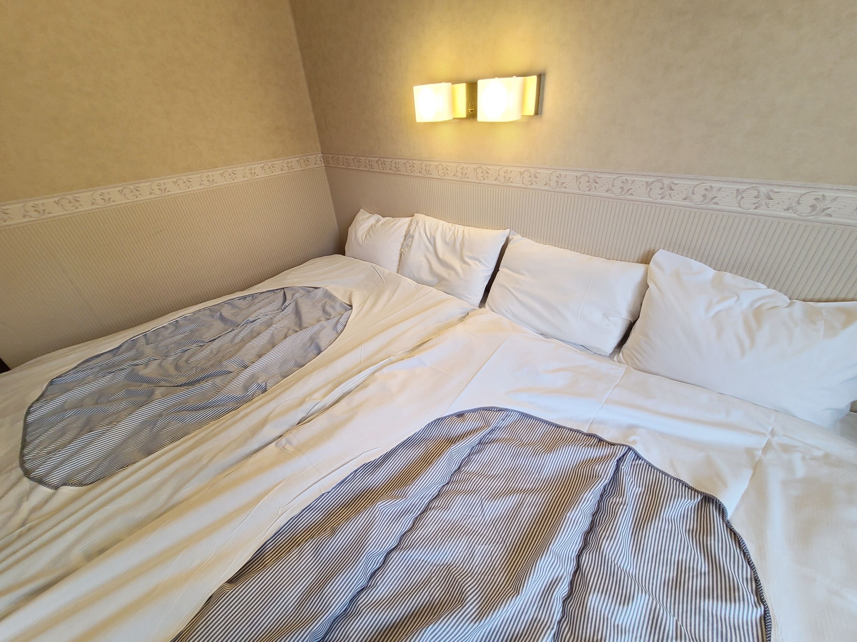 A hotel room with a bed, white bedding, and a wall-mounted light fixture.