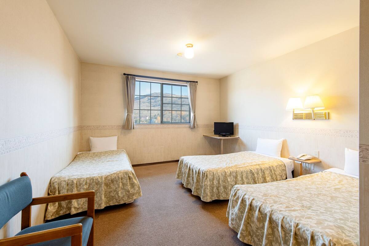 Ein Hotelzimmer mit zwei Einzelbetten, einem Fernseher, einem Schreibtisch und einem Stuhl.