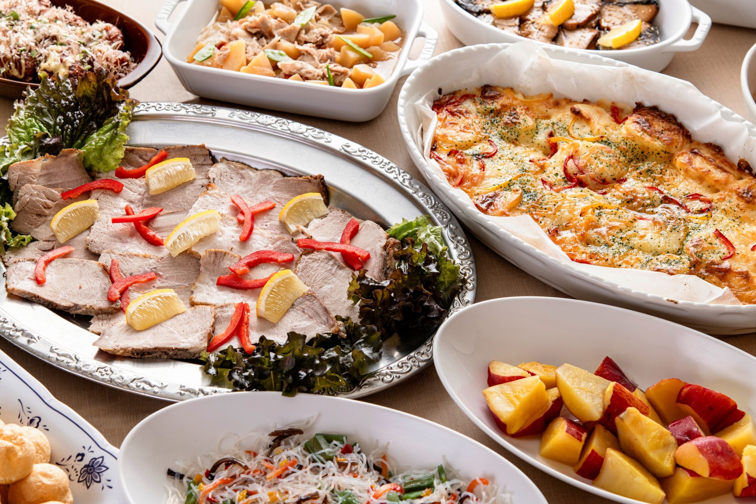 A variety of dishes including sliced meat, a baked dish, and fruit.