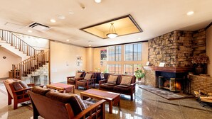 Un hall amplio con chimenea, asientos cómodos, una escalera y ventanas grandes.