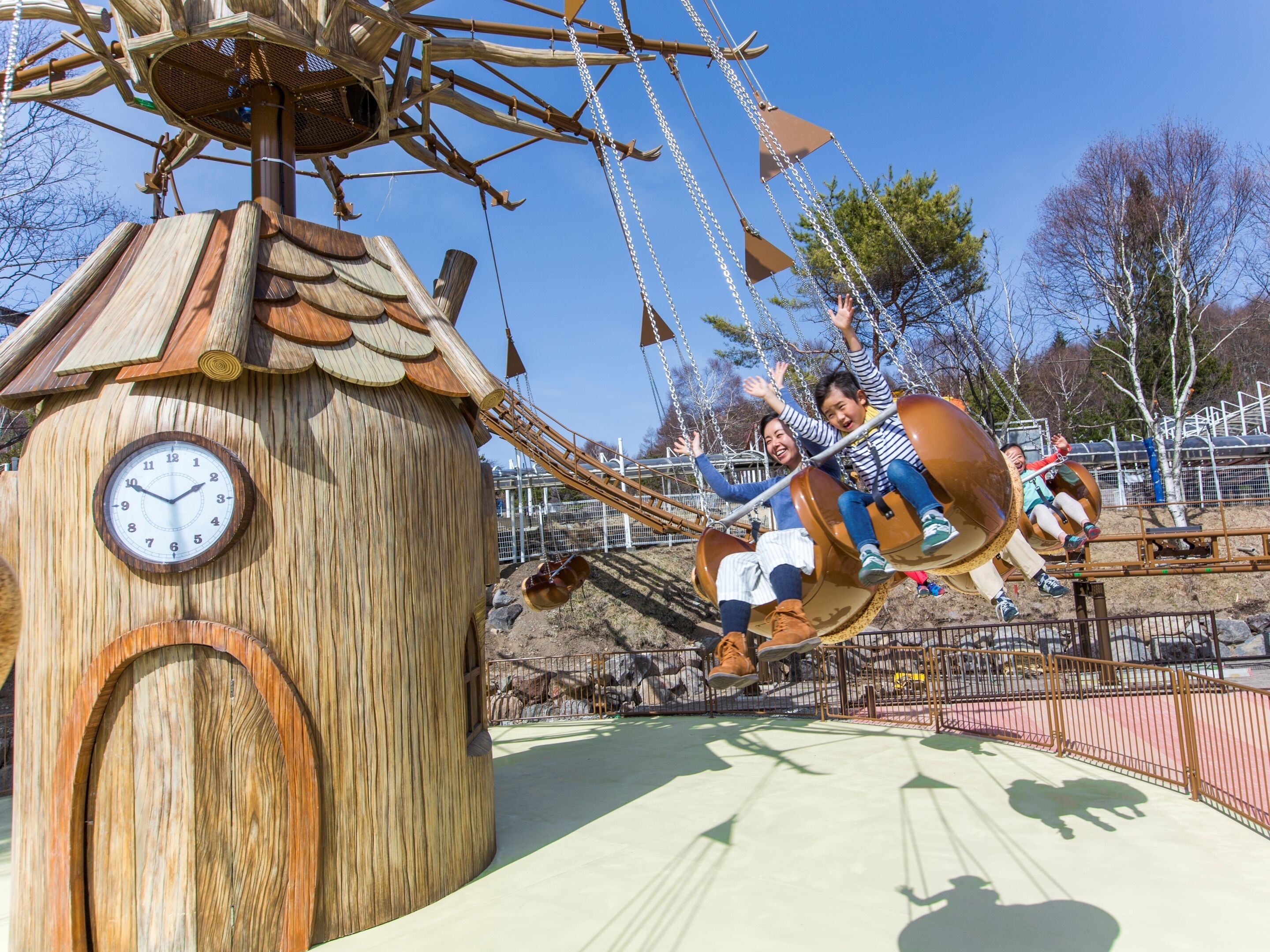 A wooden structure with a clock, a swing ride, and a fenced area.