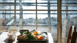Una bandeja de desayuno con cruasanes, un tazón de ensalada y un plato de fruta sobre una mesa junto a una ventana con vistas a un paisaje nevado.