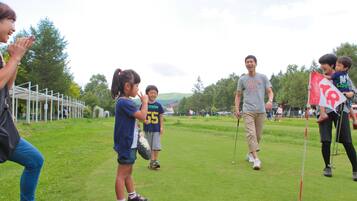 A group of people on a grassy field with a golf course in the background.
