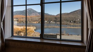 Vista a través de una ventana con diseño de cuadrícula, que da a un lago, montañas y un pequeño pueblo.