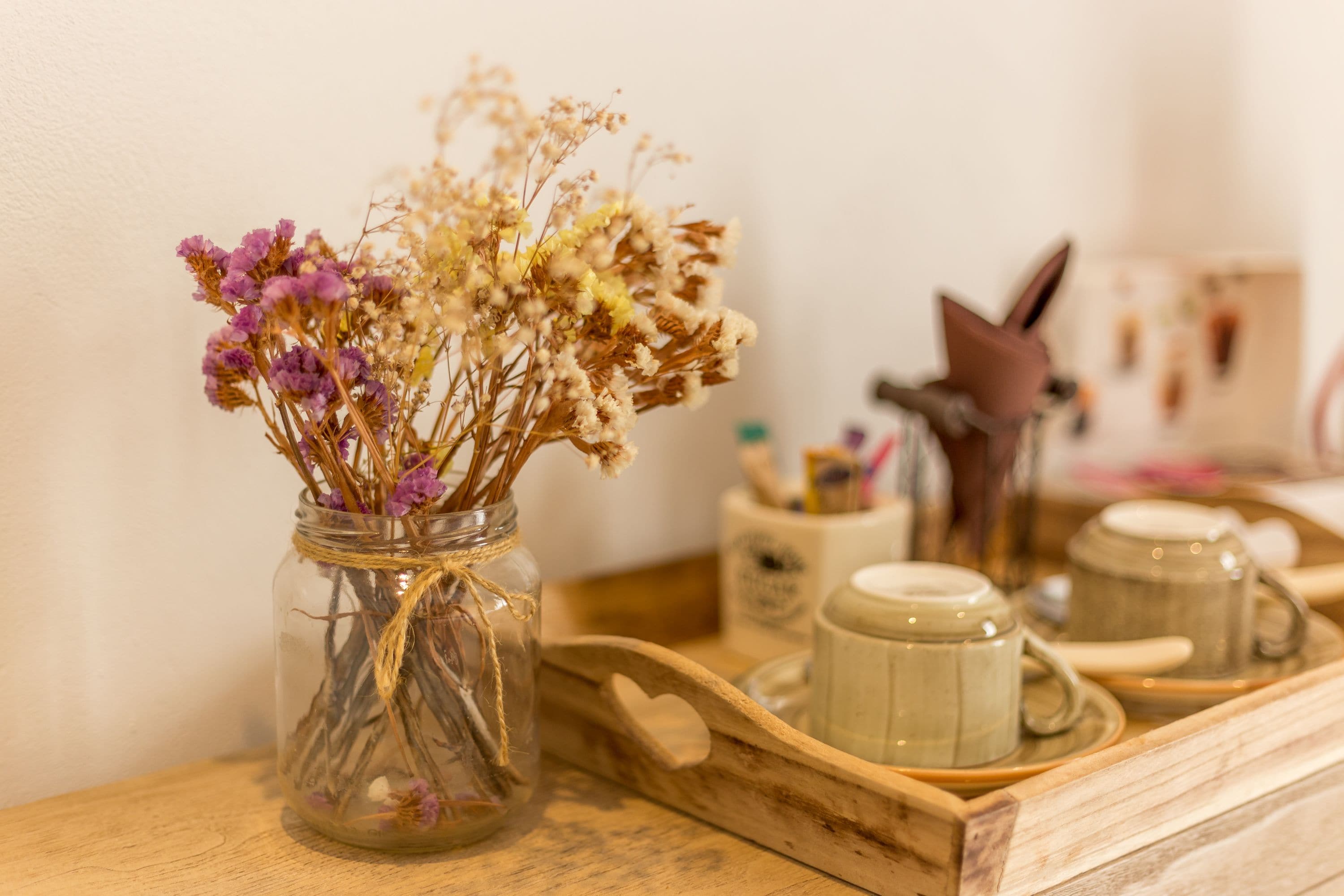 A wooden tray with a glass jar containing dried flowers and a ceramic mug.