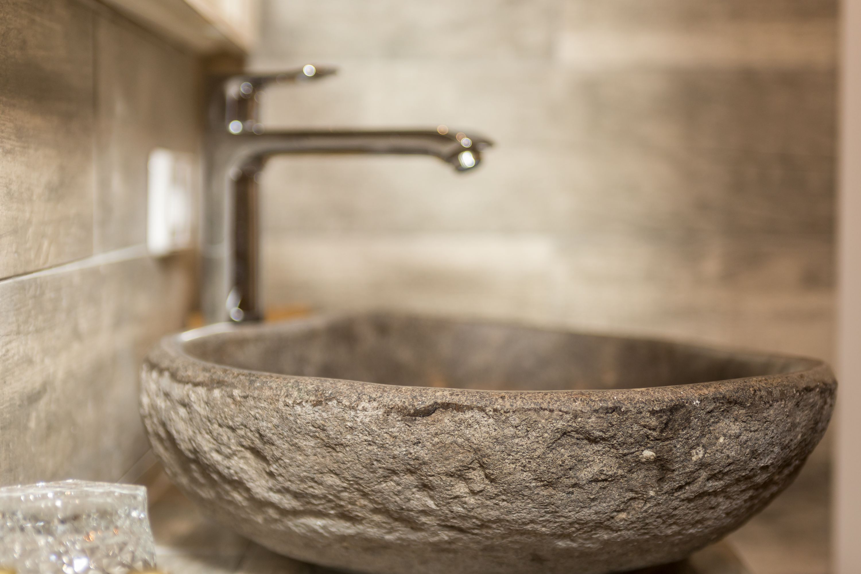 A stone basin with a modern faucet, set against a tiled wall.