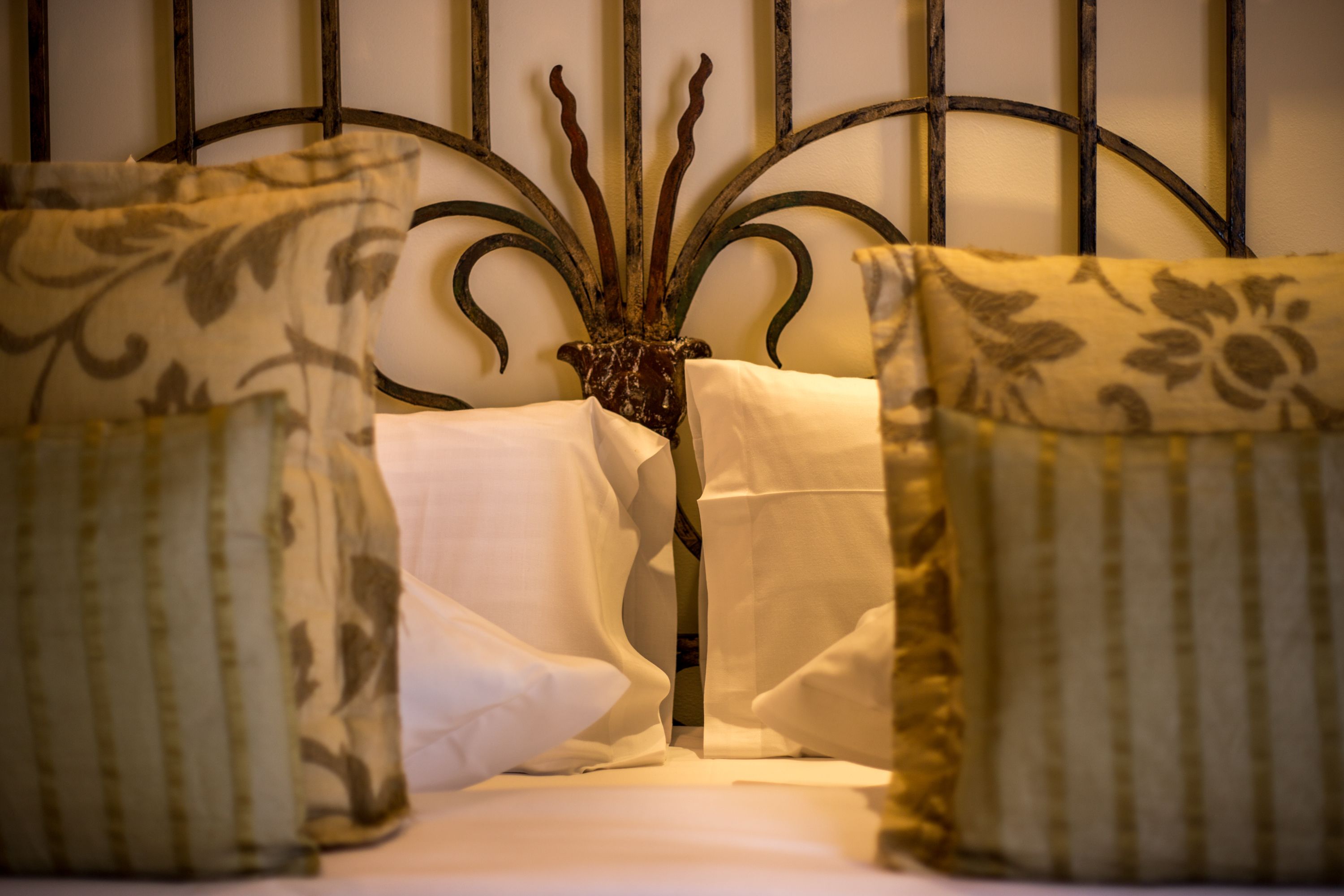 Una cama con cabecera de metal, ropa de cama blanca y almohadas estampadas.