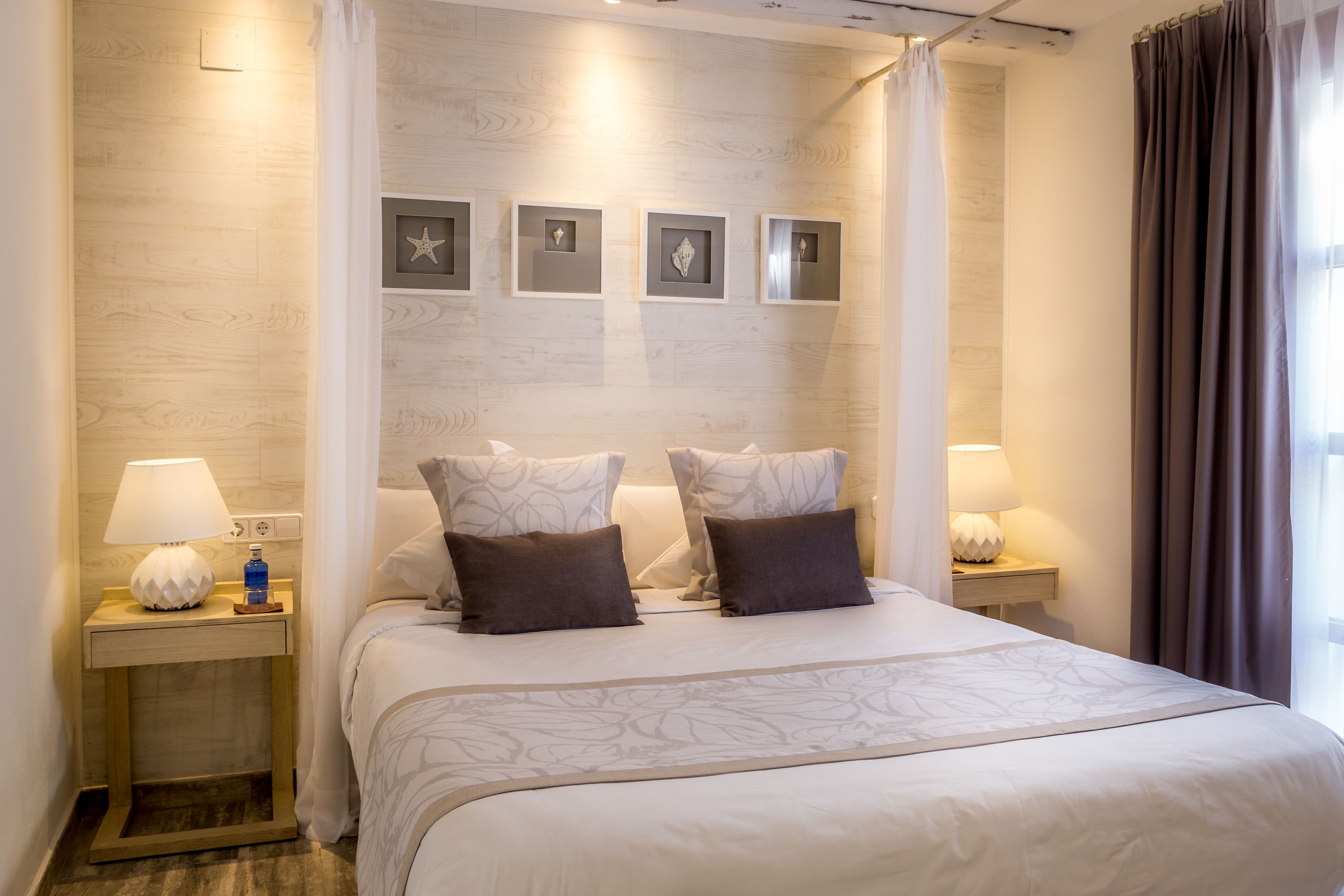 Une chambre d’hôtel avec un grand lit, deux tables de chevet avec des lampes, un cadre photo fixé au mur et un rideau.