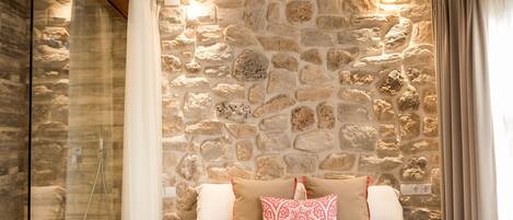 A bedroom with a stone wall, a bed with white and red bedding, and a shower area.