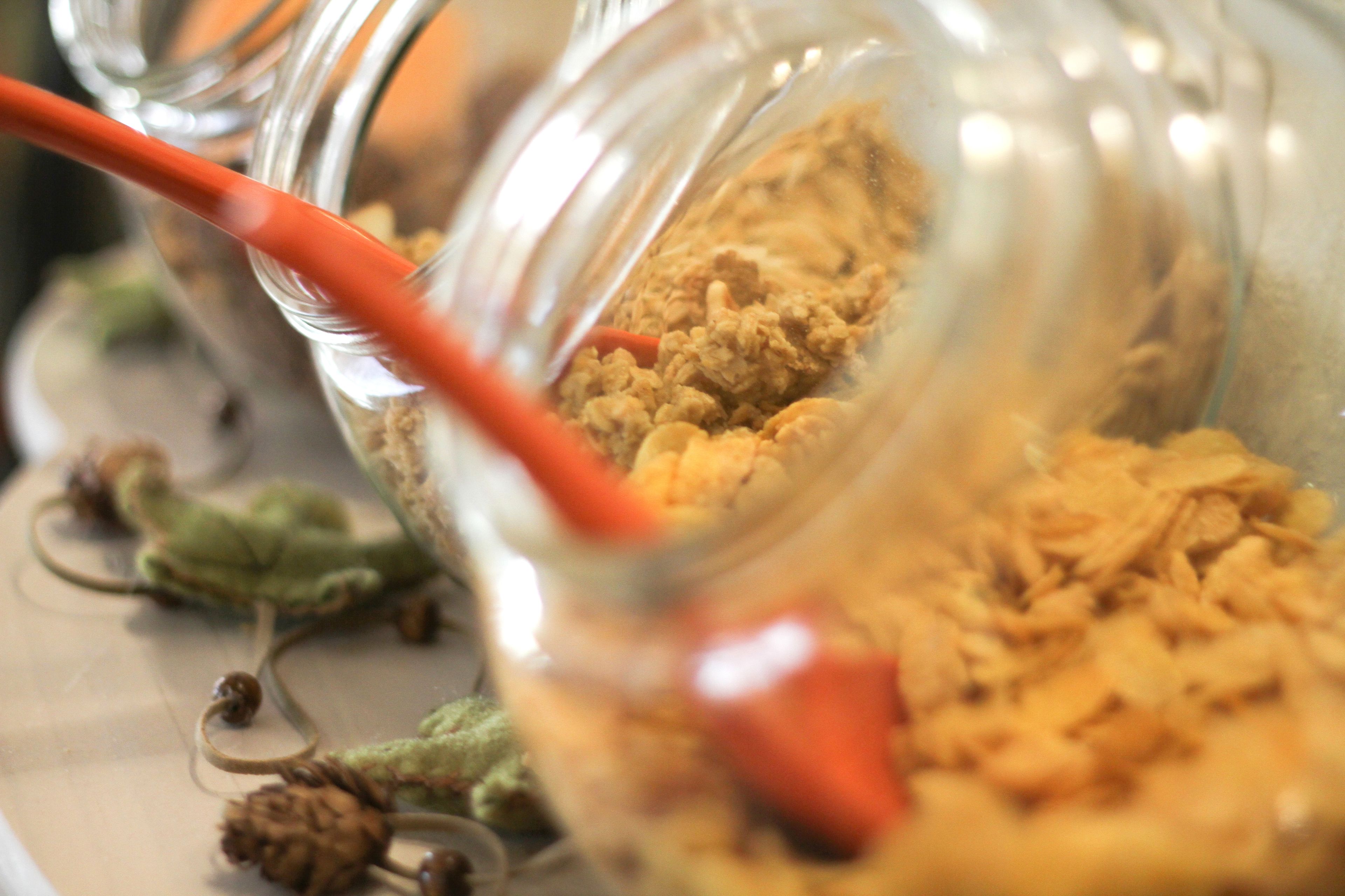 A close-up of a glass jar with a red straw, containing a granular substance, possibly food, with a blurred background.