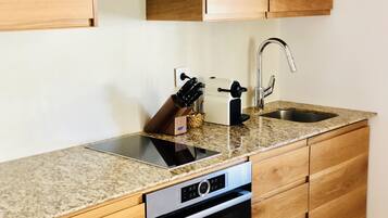 Una cocina con gabinetes de madera, un lavamanos de acero inoxidable, un horno empotrado y una cafetera.