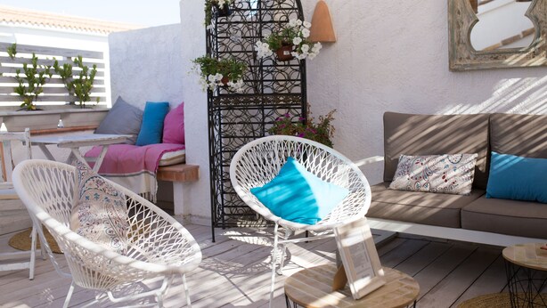 A terrace with wicker chairs, a sofa, and a table. There is a decorative metal gate with flowers and a wall-mounted mirror. - Hotel Ábaco Altea (Altea)