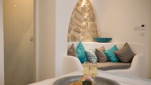 A modern room with a stone wall, a white sofa with patterned cushions, and a table with a plate of food. - Hotel Ábaco Altea (Altea)