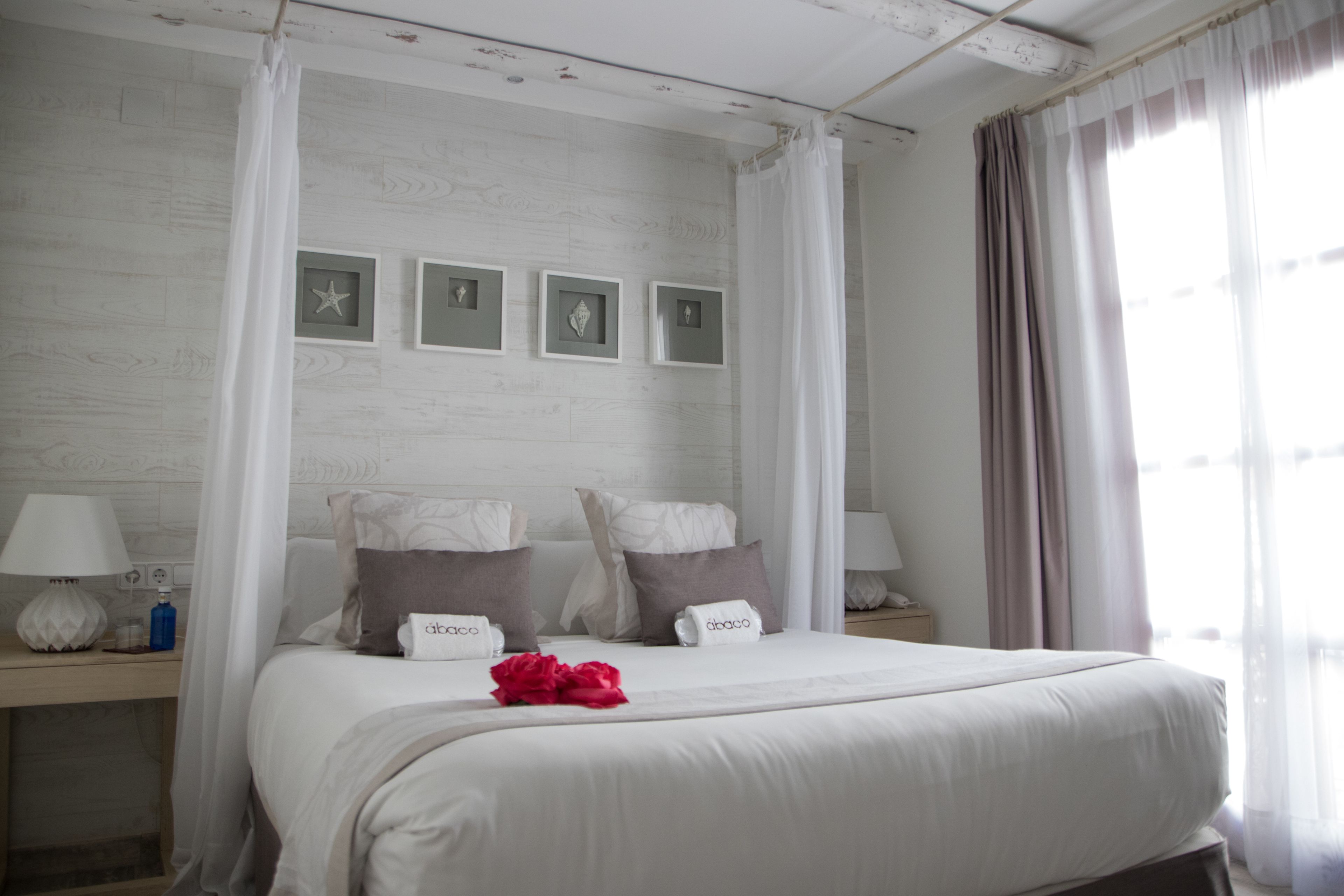 Une chambre à coucher comprenant un lit, deux tables de chevet, une commode, une fenêtre avec des rideaux et des cadres photo accrochés au mur.