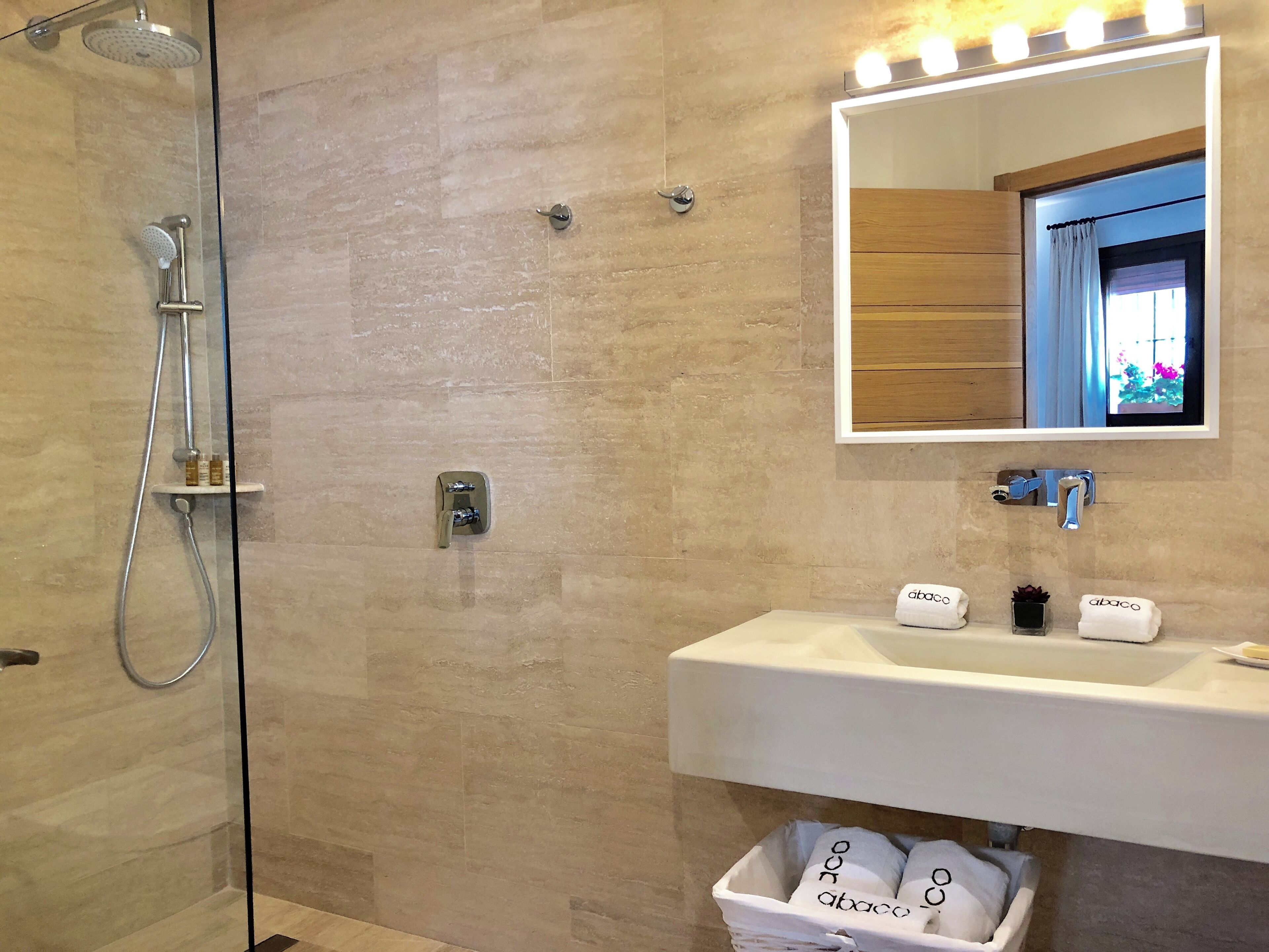 A modern bathroom with a glass-enclosed shower, a white sink, and a mirror with lights above it.