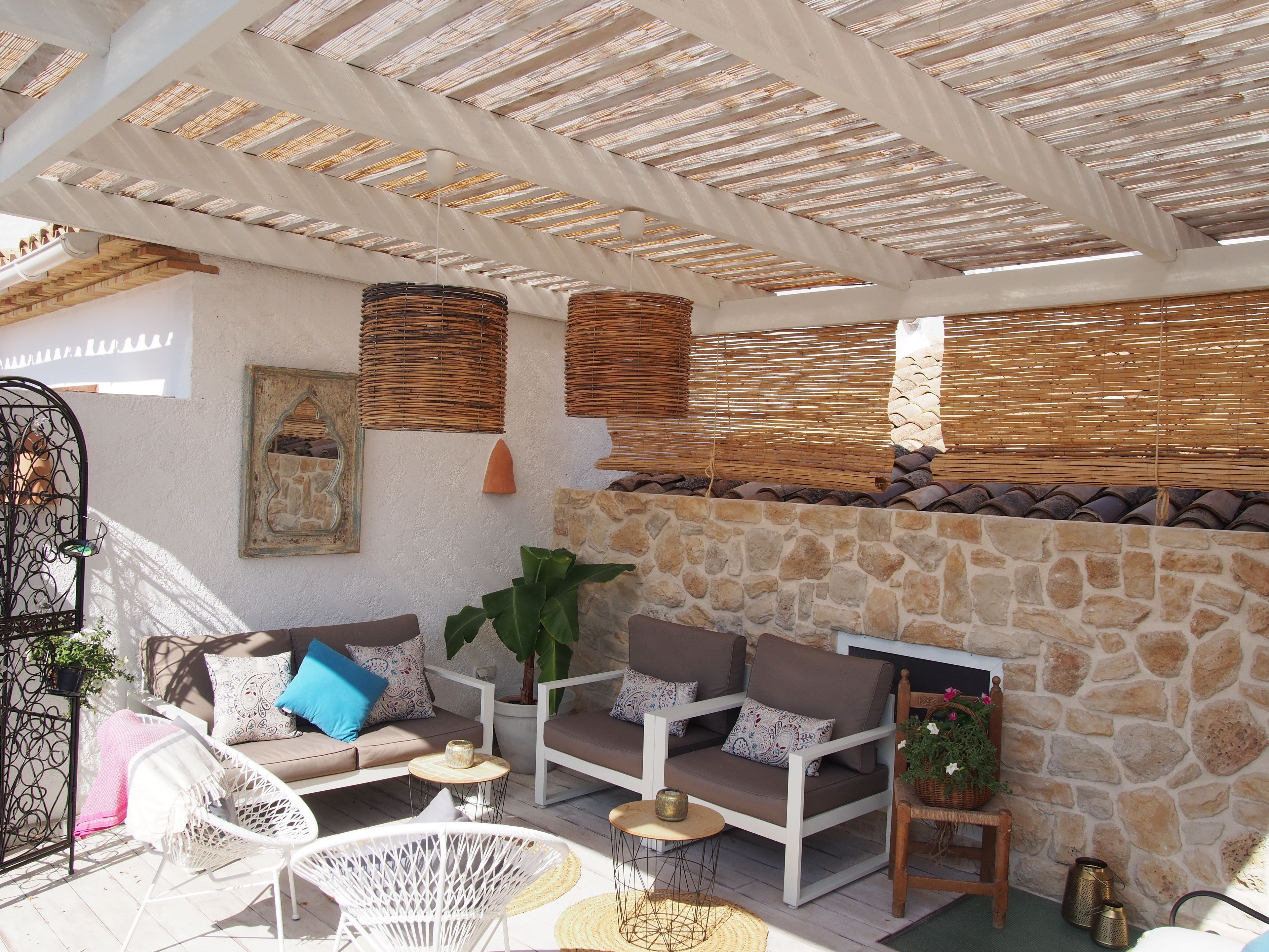 An outdoor seating area with stone walls, wicker blinds, and a variety of seating options including sofas and chairs.