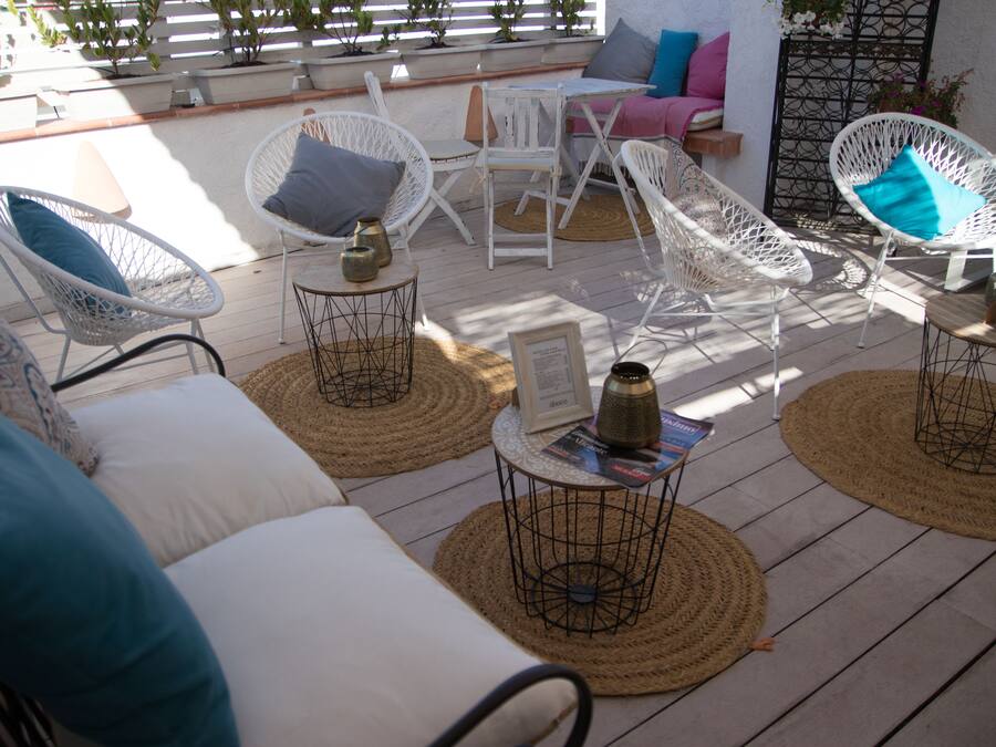 Un patio iluminado por el sol con sillas de mimbre blanco, esteras tejidas y una mesita con una revista.