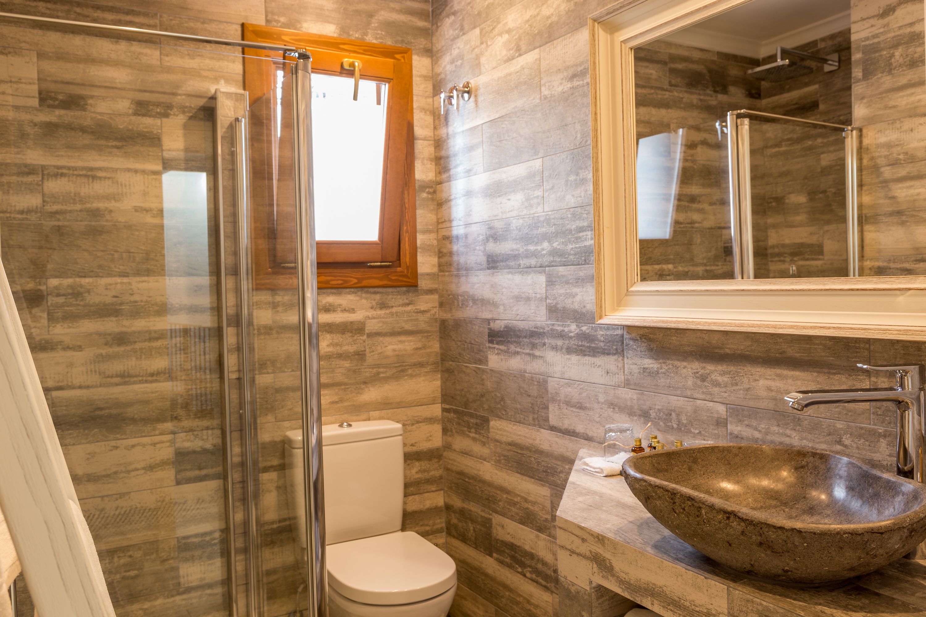 Un baño con cabina de ducha de vidrio, inodoro y un lavamanos de piedra grande.