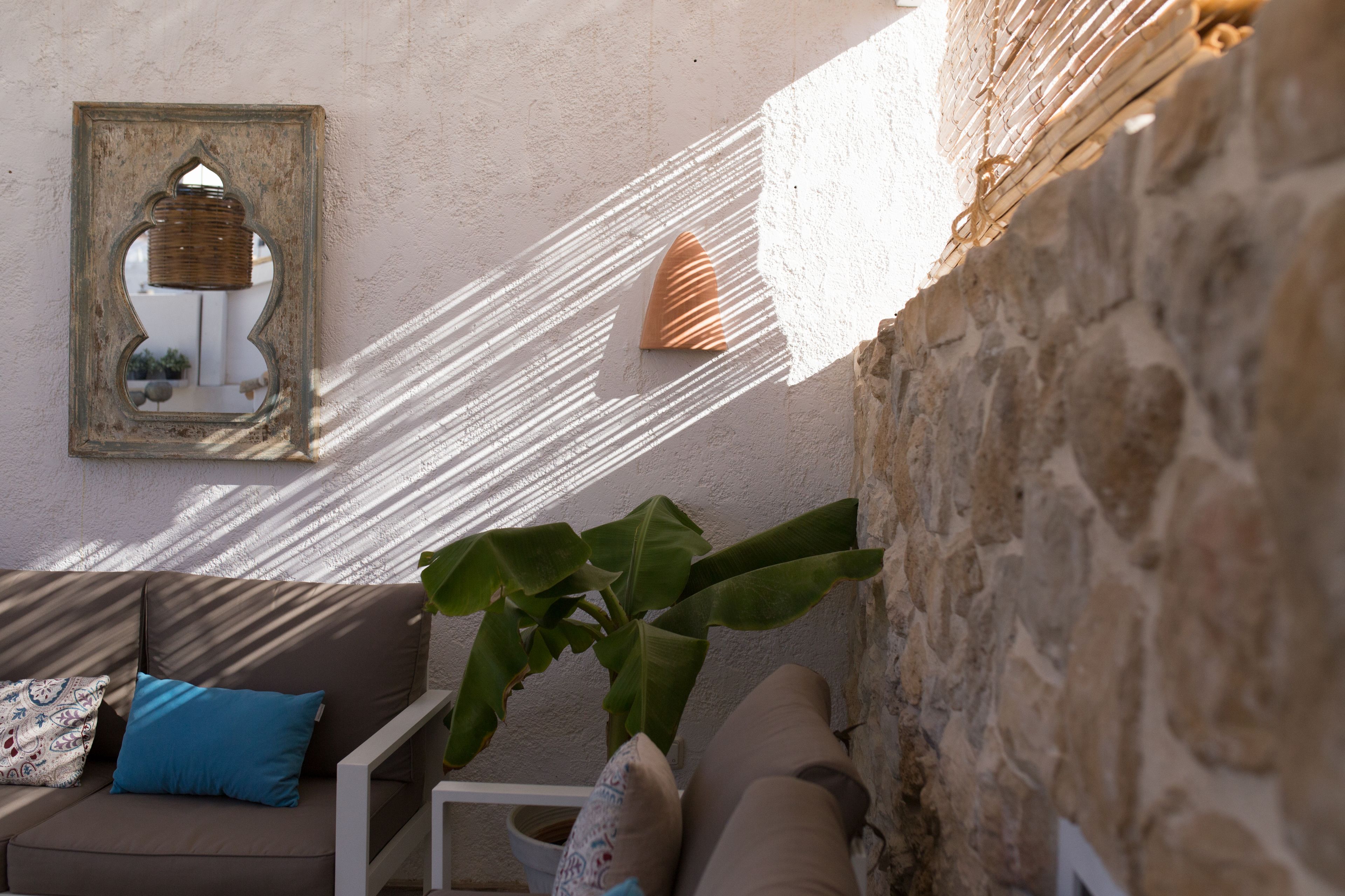 Un espacio al aire libre iluminado por el sol, con pared de piedra, cesta de mimbre y sofá acolchado con almohada azul.