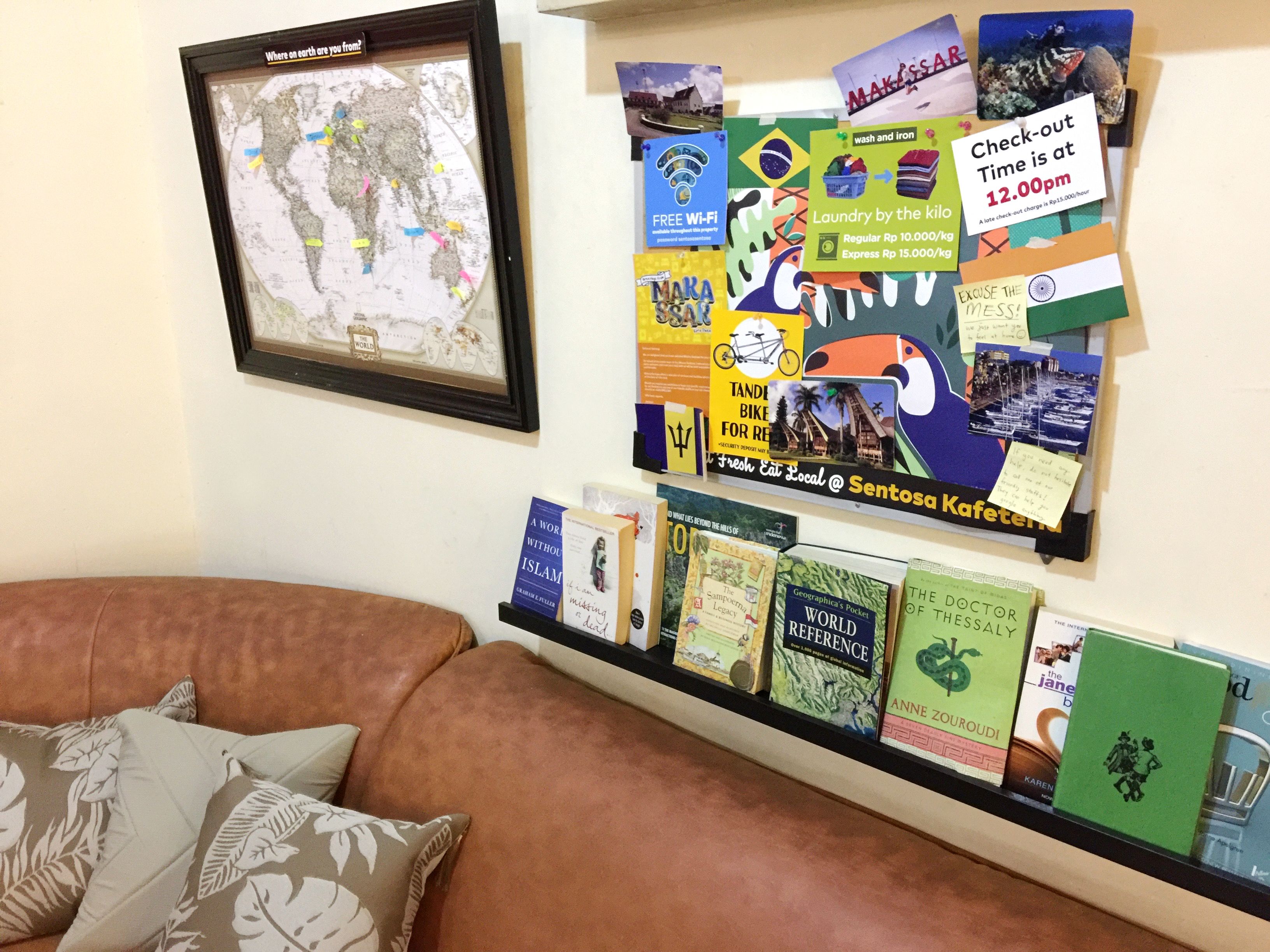 A wall with a framed map, a bulletin board with various notes and pictures, and a bookshelf with books.