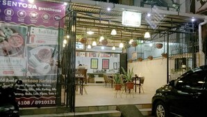 A guesthouse with a signboard advertising services like laundry and in-house showers. There are tables and chairs arranged outside, and a car is parked nearby. - Wisma Sentosa (Makassar)