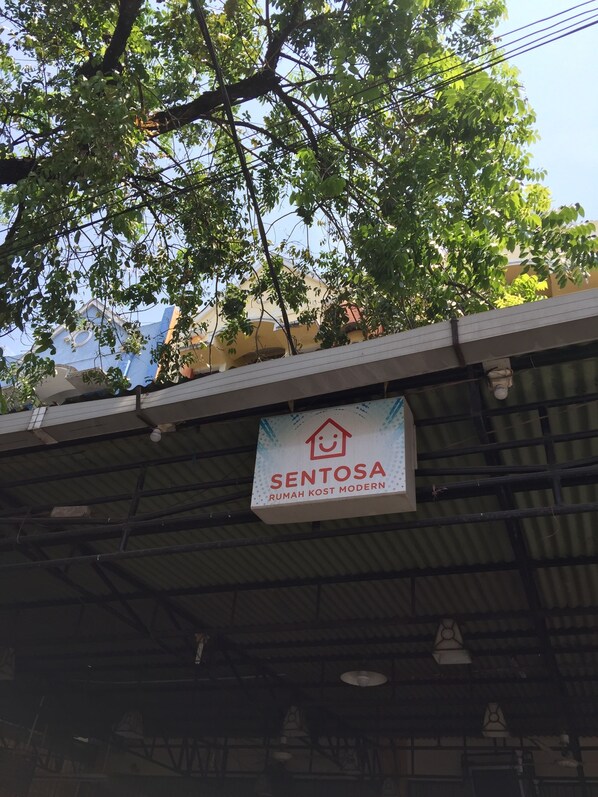 A sign for 'SENTOSA Rumah Kost Modern' hanging on a building's roof.