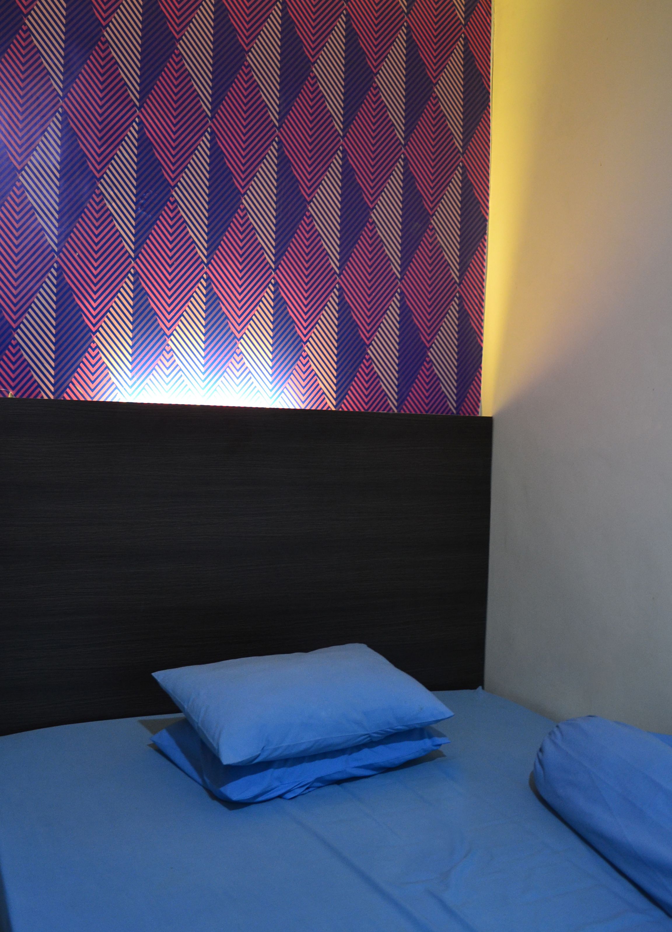 Un lit avec un matelas et des oreillers bleus, une tête de lit sombre et un mur à motifs avec des lignes diagonales.