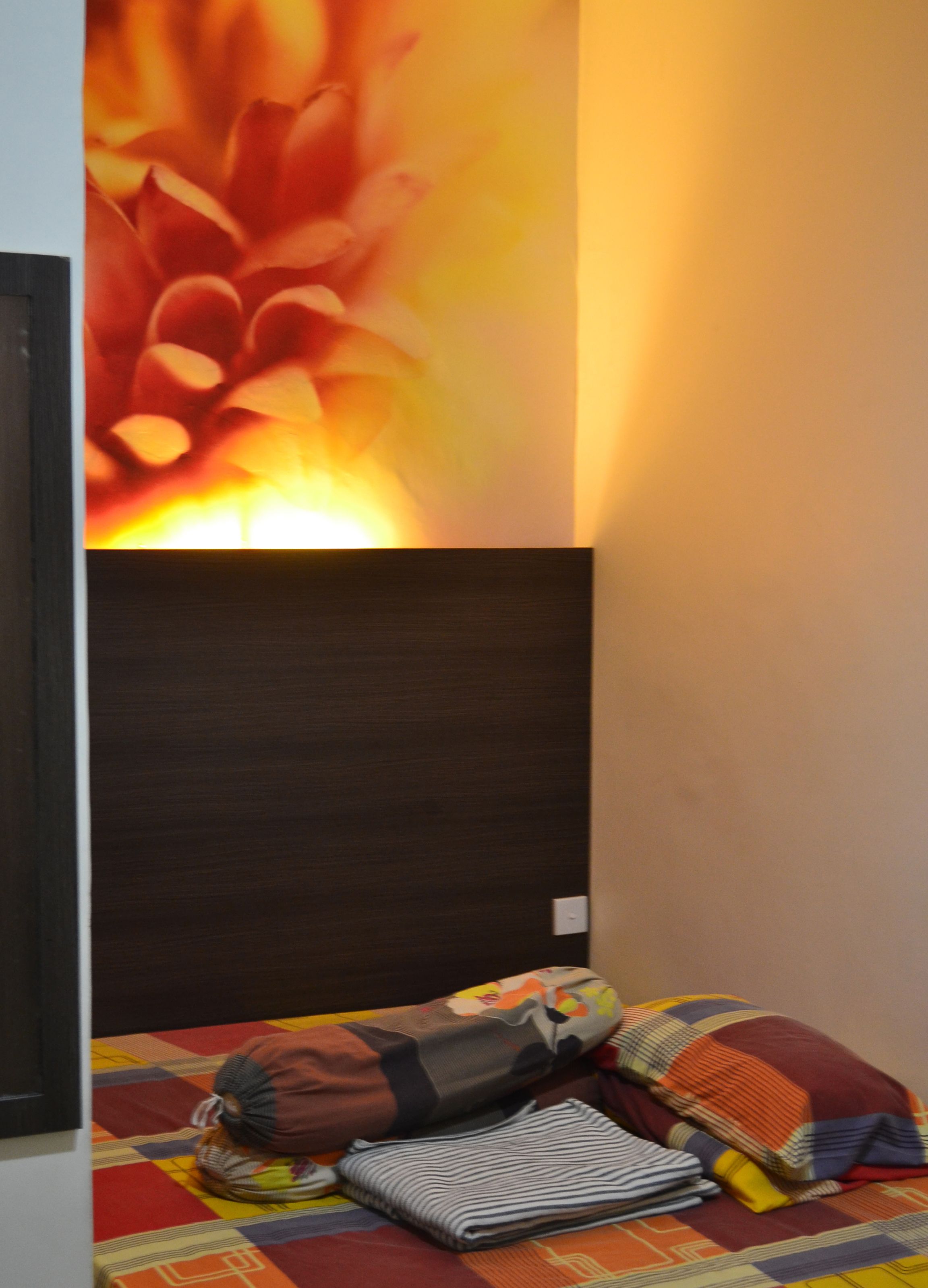 A hotel room with a dark headboard, a colorful quilted bedspread, and a wall with a large floral mural.