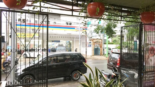 A gas station with a black car parked in front, potted plants, and a metal gate. - Wisma Sentosa (Makassar)
