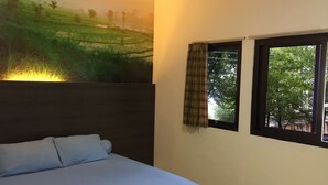 A bedroom with a bed, a large wall mural of a landscape, and a window with curtains. - Wisma Sentosa (Makassar)