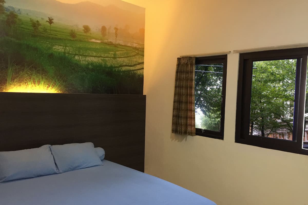 A bedroom with a bed, a large wall mural of a landscape, and a window with curtains.