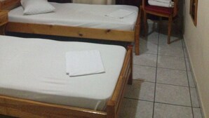 A room with two single beds, a chair, a window with curtains, and a wall-mounted light fixture. - Ikaros Hotel (Piraeus)