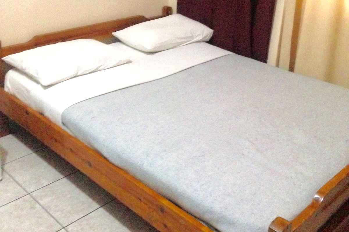 A single bed with a wooden frame, white bedding, and a wall-mounted light fixture.
