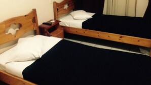 A room with two wooden beds, each with a white pillow and black bedspread. There is a nightstand with a remote control and a lamp on the wall. - Ikaros Hotel (Piraeus)