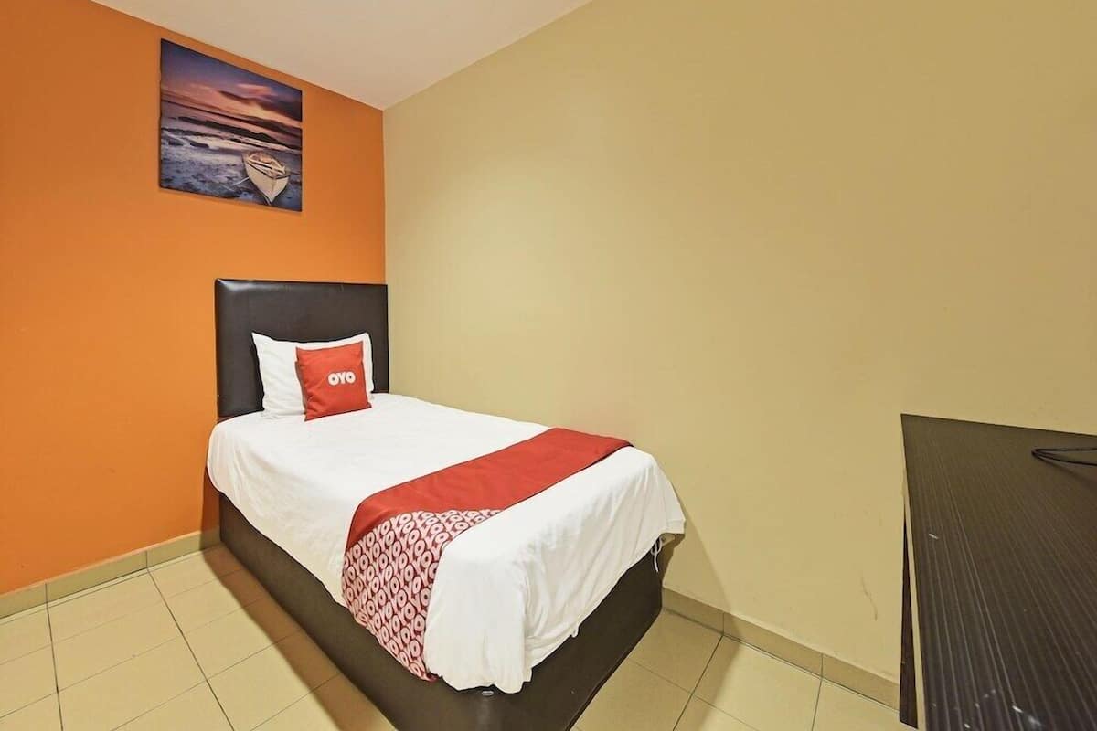 A single bed with a headboard, a red pillow, and a white bedspread.