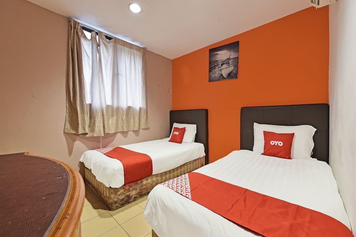 A hotel room with two beds, a window with curtains, a painting on the wall, and a round table.