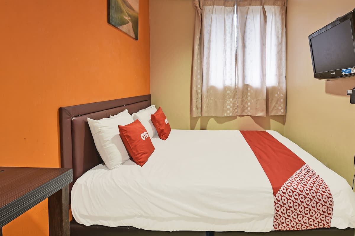 A hotel room with a bed, two pillows, a TV, and a window with curtains.