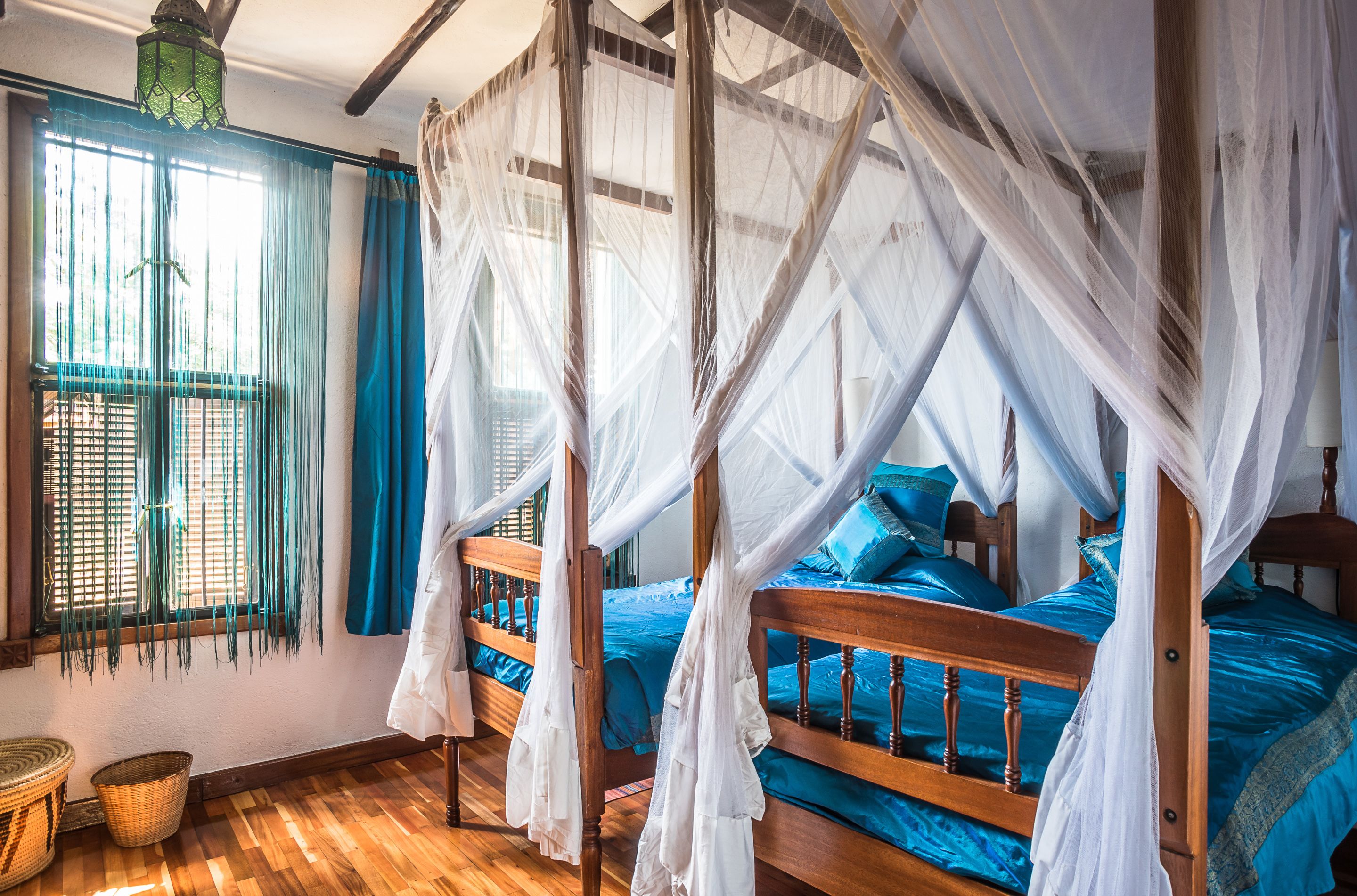 A room with a wooden bed, blue bedding, and a window with blue curtains.