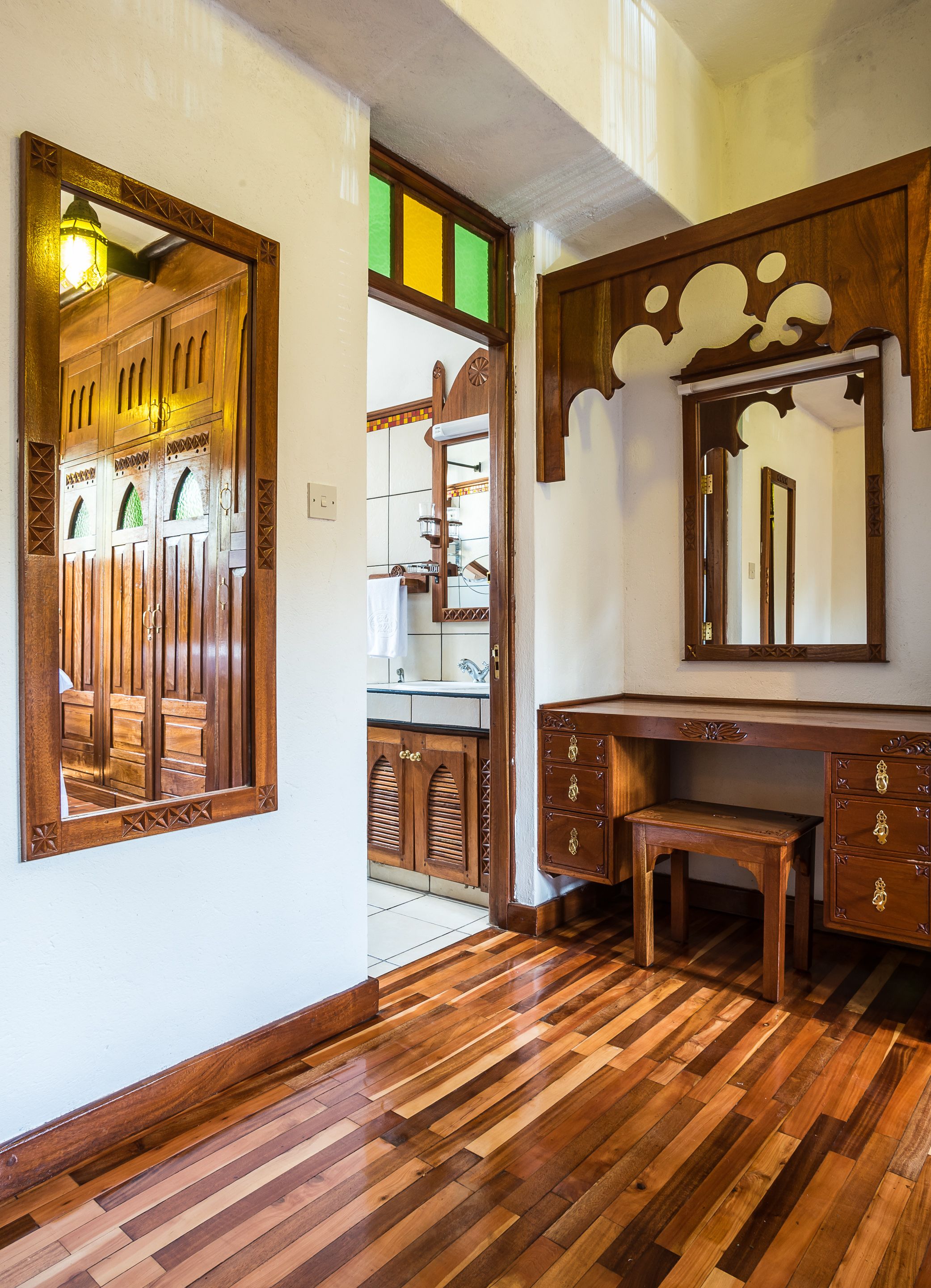 A room with wooden flooring, a wooden desk with drawers, a mirror, and a cabinet with a tiled backsplash.