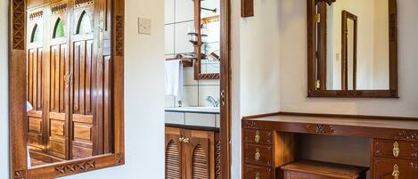 Una habitación con suelo de madera, un escritorio de madera con cajones, un espejo y un mueble con salpicadero de azulejos.