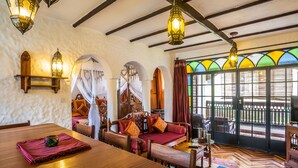 A cozy room with a wooden dining table, cushioned seating, and a large window with colorful stained glass. - The King Post (Nairobi)
