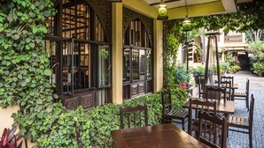 An outdoor patio with wooden tables and chairs, surrounded by lush greenery and traditional architectural elements. - The King Post (Nairobi)