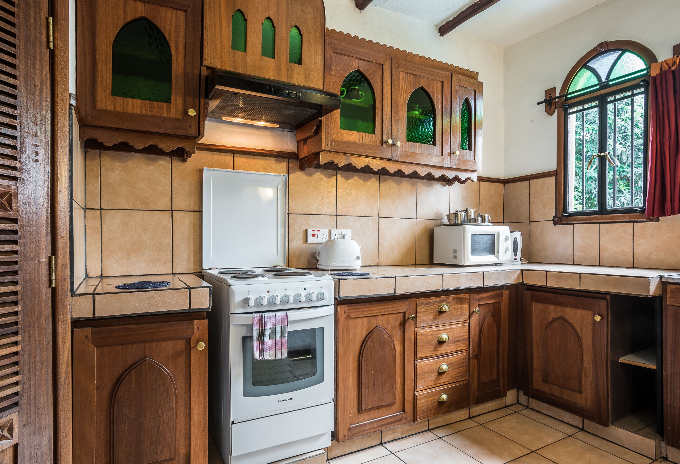A kitchen with wooden cabinets, a stove, a microwave, and a window with curtains.